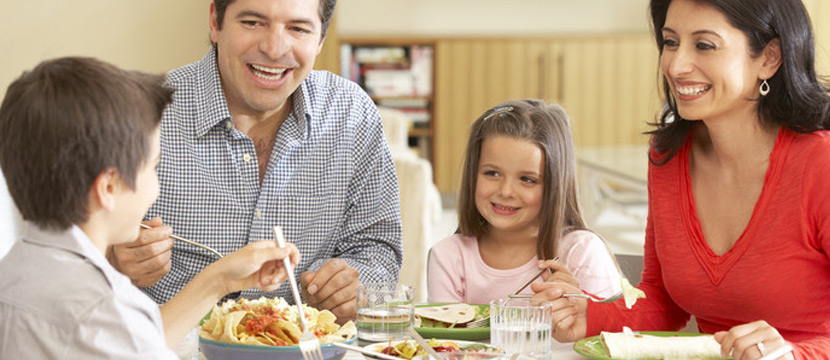 Parents with their young kids including a small boy and a girl eating dinner at the dinner table.