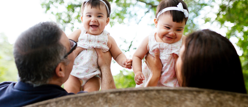 Parents sitting on the bench and holding their smiling twin babies up in the air.