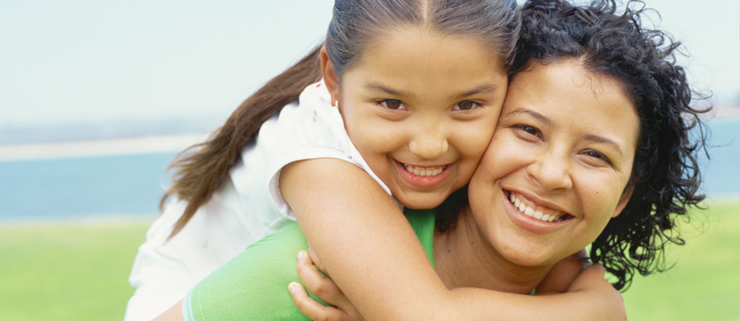 Young girl hugging her mom and both of them are smiling and looking at the camera.